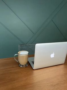 an apple laptop computer sitting on top of a wooden table next to a cup of coffee