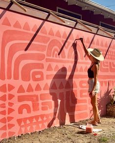 a woman is painting the side of a wall with pink and white designs on it