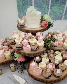 cupcakes are arranged on wooden slices with pink and white frosting, along with greenery