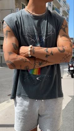 a man with tattoos on his arms and chest standing in front of a street corner