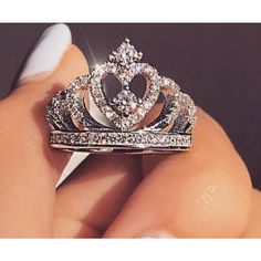 a close up of a person's hand holding a ring with a tiara on it