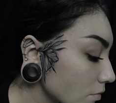 a woman with ear piercings on her face and behind her ear is a bird