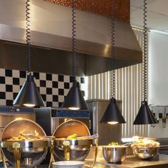 a restaurant kitchen with lots of food on the counter and hanging lights above it that are black and white checkered wallpaper