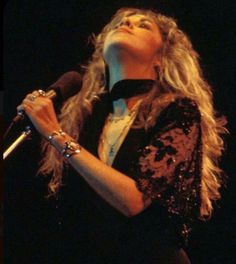 a woman holding a microphone in her right hand and wearing a black top with sequins on it