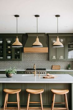 three stools sit in front of an island with two lights hanging over it and green cabinets