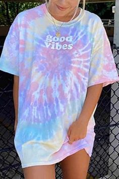 a woman wearing a tie dye shirt and shorts standing in front of a chain link fence