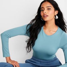 a woman sitting on the ground with her hands behind her back, wearing blue pants and a long sleeved top