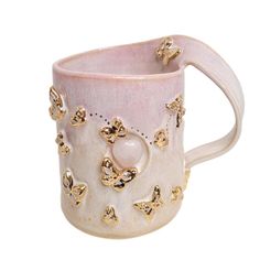 a pink and white coffee cup with gold butterflies on the side, in front of a white background