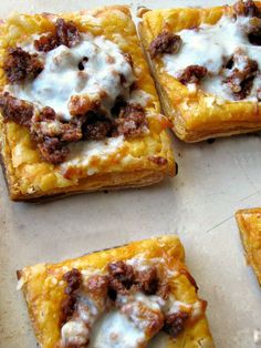 four square pieces of pizza with cheese and meat toppings on top, sitting on a baking sheet