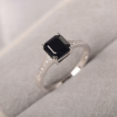 a black diamond ring sitting on top of a white cloth covered box with diamonds around it