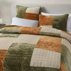 a bed with green and brown bedspread, pillows and blankets on top of it