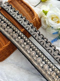 two pieces of black and gold beaded ribbon next to a wicker basket with flowers