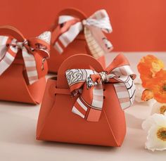 two red purses with bows on them sitting next to some white and orange flowers