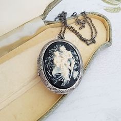 Classical style Victorian inspired large cameo locket necklace in black and cream. The detailed cameo has a black background, and is set on a large opening locket in gunmetal or antiqued bronze plated on a matching chain. The locket will hold two photos (approx the same size as the cameo), or any small precious object.  The locket measures just under 2 inches (50mm) from top to bottom, and the matching chain is has a lobster clasp. The chain length can be altered at no extra cost. Choose gunmetal plated or antiqued bronze plated. This necklace comes in a gift box. Antique Cameo Necklace Keepsake, Antique Cameo Necklace As Keepsake, Vintage Black Locket Necklace, Antique Cameo Necklace For Keepsake, Black Cameo Medallion Jewelry, Cameo Medallion Necklace For Keepsake, Vintage Black Cameo Necklace, Black Cameo Jewelry For Collectors, Black Cameo Necklace In Vintage Style