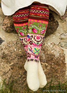 a woman's legs with colorful socks and flowers on them sitting in front of a stone wall