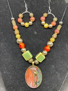 Unique Fluid art pendant and earrings, featuring greens and red in antique brass setting . This pendant is made from acrylic paint that dripped from my pour paintings. The paint dries and makes a skin which is positioned under a glass cabochon and then placed into the nickel free stainless steel bezel. The statement piece is in shades of red and green and the beads complement the colors, all in an antique brass setting. Earrings match. Color is my passion and each is unique in its own way. Beads are glass and plastic and the cord is wax coated. The length is adjustable with a sliding knot. Acrylic Pour Jewelry, Unique Multicolor Brass Jewelry, Artsy Resin Dangle Jewelry, Artistic Resin Dangle Jewelry, Multicolor Copper Jewelry Gift, Hand Painted Artsy Resin Jewelry, Multicolor Copper Jewelry For Gift, Multicolor Copper Jewelry For Gifts, Artsy Hand Painted Resin Jewelry