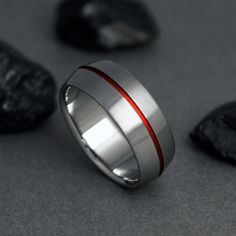 a silver ring with a red stripe on the side and black rocks in the background