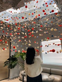 a woman standing in front of a window looking at flowers hanging from the ceiling