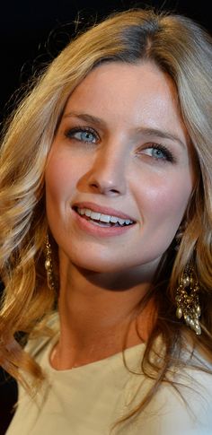 a close up of a woman with blonde hair and blue eyes wearing large gold earrings