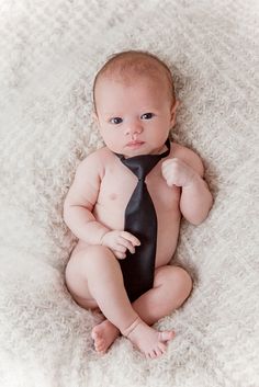 a baby wearing a black tie on top of a white blanket