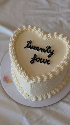 a heart shaped cake with writing on the top is sitting on a white tablecloth