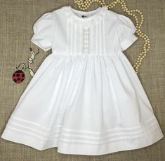 This Gorgeous White Dress will be perfect for your little one's Christening Dress, Baptism Dress, Flower Girl Dress or any special occasion. It comes with a Cotton Blommer. FABRIC: Spichler Vogel Pima 100% Cotton . SPECIAL FEATURES: The front Yoke is beautifully cover with a delicate vertical Cotton insertion, and 3 sets of vertical spaced tucks on each side of the Lace insertion. It has beautiful white Lace trim around the Neckline . Puffed short sleeves with cuffs. The end of the skirt is ador Elegant First Communion Dress For Summer Confirmation, Elegant Fitted Baptism Dress For Dress-up, Elegant Fitted Baptism Dress For Spring, Classic Short Sleeve Dress For Baptism, Short Sleeve Fitted Baptism Dress, Elegant Short Sleeve First Communion Summer Dress, Classic Fitted Dress For Baptism, Fitted First Communion Dress For Summer Dress-up, Fitted Summer First Communion Dress