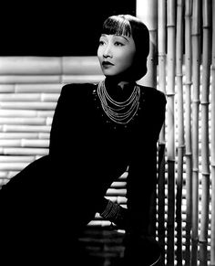 a woman sitting on top of a chair next to a bamboo wall and wearing a necklace