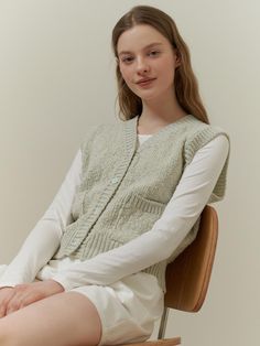 The garment is a sleeveless knitted vest with a V-neckline and front button closure. The knit texture is prominently visible, indicating a cozy, tactile feel. It also features ribbed detailing along the neckline, armholes, and hem, providing a neat and finished look.- The vest includes two front pockets which add practicality and a casual element to the design.- Its relaxed fit suggests it can be layered over various outfits for added warmth.- The ribbed details enhance the fit and contribute to the vest's classic style. Casual Knit Vest With Button Closure, Casual Sleeveless Button Cardigan, Sleeveless Knit Sweater Vest With Buttons, Sleeveless Knit Vest With Button Closure, Casual Sleeveless Cardigan With Button Closure, Casual Knit Sweater Vest With Button Closure, Winter Knit Sweater Vest With Button Closure, Spring Knit Sweater Vest With Button Closure, Knit Sweater Vest With Button Closure For Spring