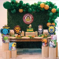 a table topped with lots of cake and balloons in front of a wall covered in greenery