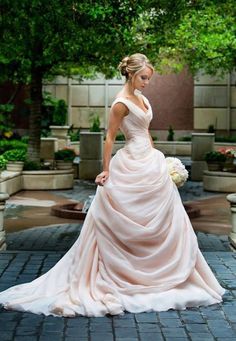 a woman in a wedding dress is standing on a brick walkway with trees and bushes behind her