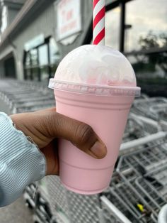 a hand holding a pink cup with whipped cream and a red striped straw in it