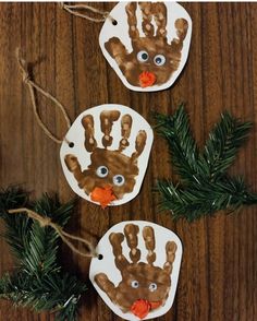 three handprinted christmas ornaments hanging from twine on a wooden table with pine branches