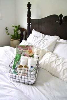 a bed with white linens and a basket filled with books sitting on top of it