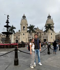 a man and woman standing in front of a large building with statues on the sides