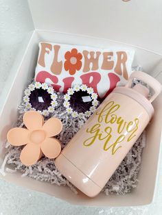 a pink water bottle and sunglasses in a white box with flowers on the lid next to a pair of eyeglasses