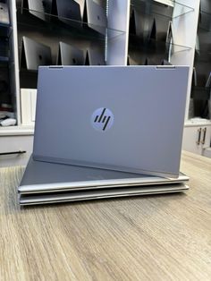 two laptops sitting on top of each other on a wooden table in front of shelves