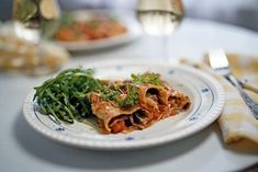 a white plate topped with lasagna covered in sauce and veggies next to a glass of wine