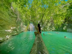 a woman sitting on top of a log in the middle of a river next to a waterfall