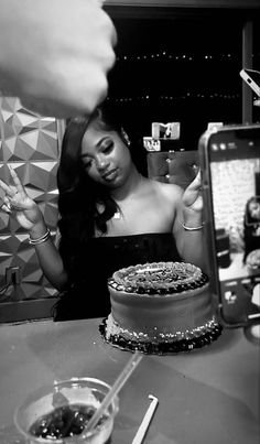 a woman is looking at her cell phone while sitting in front of a cake