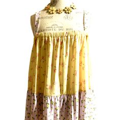 a yellow and pink dress with flowers on the bottom is hanging from a mannequin