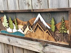 a wooden wall hanging with mountains and trees on it