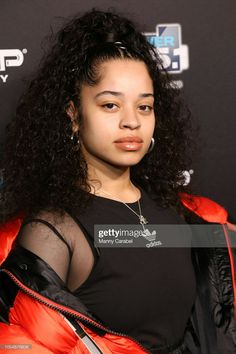 an image of a woman with long curly hair wearing a black top and red jacket