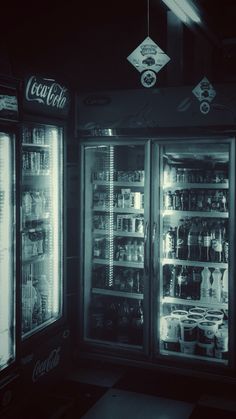 two refrigerators with drinks and beverages in them are lit by lights from overhead lamps