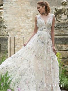 a woman wearing a dress with flowers on it and standing in front of a stone wall