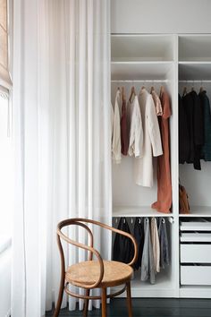 an open closet with clothes hanging on the wall and a chair in front of it