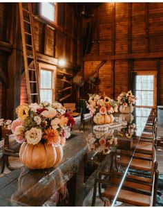 a table with flowers and pumpkins on it in front of a wooden wall that has stairs