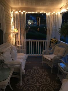 a porch with white wicker furniture and string lights on the windowsill, along with curtains