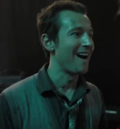 a man laughing while wearing a green shirt and black tie in front of a dark background