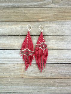 the red beaded earrings are hanging from hooks on a wooden surface with wood planks