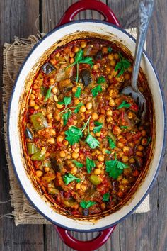 a red pot filled with baked eggplant and chickpeas on top of a wooden table